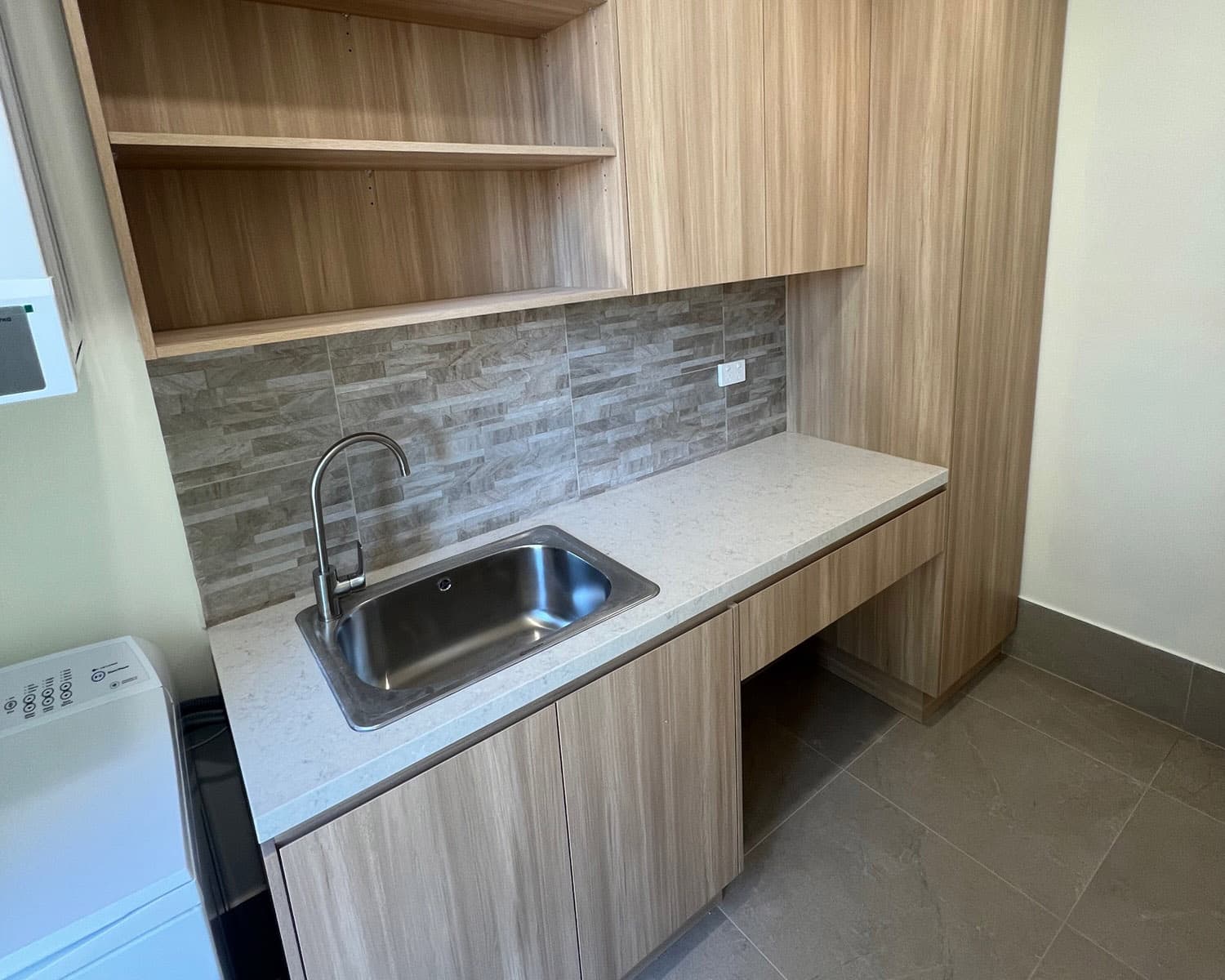 Finished laundry fit out with a new stainless sink, tapware and custom timber cabinetry over a tiled splashback, an Allspec Plumbing install
